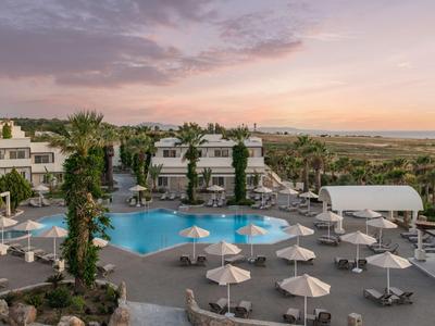 Hotel pool with loungers and umbrellas at sunset in an open landscape.