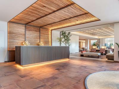 Modern hotel reception with wooden ceiling, illuminated desk, and cozy lounge area.