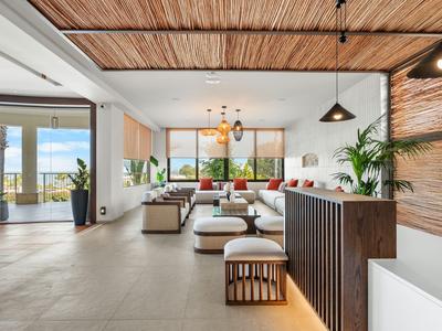 Modern hotel lobby with lounge furniture, plants, and large windows offering sea views.