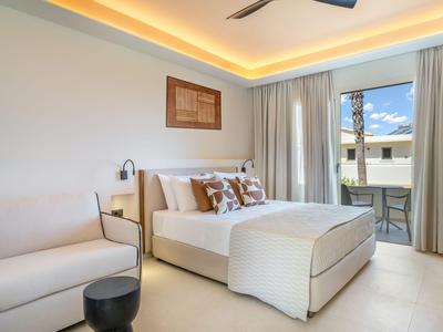 Brightly furnished hotel room with double bed, sofa, and balcony overlooking neighboring buildings.