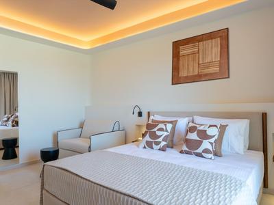 Modern hotel room with large bed, sofa, wall art, and indirect ceiling lighting.