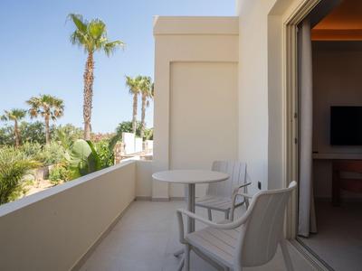 Balcony with white chairs and table, palm trees in the background, clear sky.