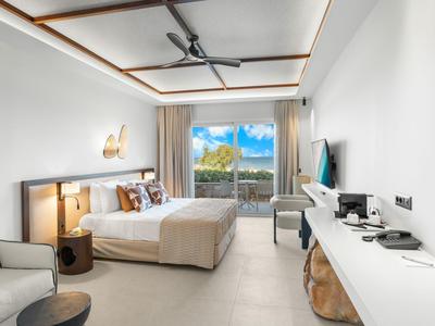 Modern hotel room with double bed, large windows, and mountain view in daylight.