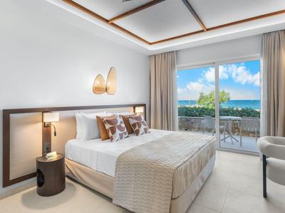 Modern hotel room with double bed, balcony, and sea view in daylight.