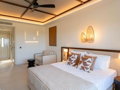 Brightly decorated hotel room with double bed, two armchairs, and a ceiling fan.