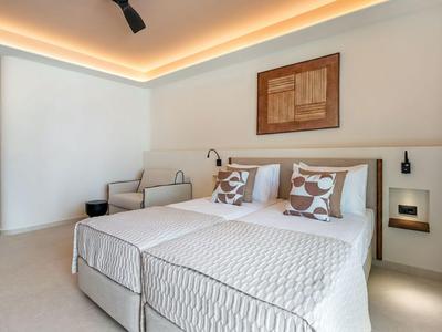 Modern hotel room with double bed, comfy armchairs, and minimalist design.