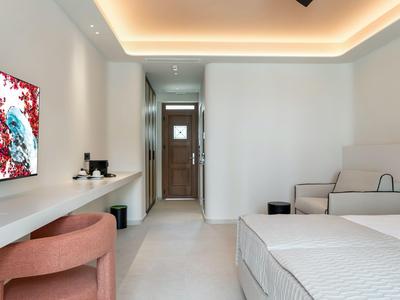 Modern hotel room with bed, TV, desk, and beige seating area.