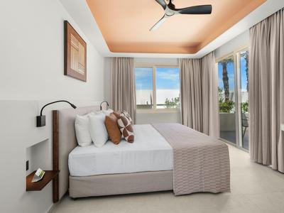 Modern hotel room with large bed, balcony, and ceiling fan.