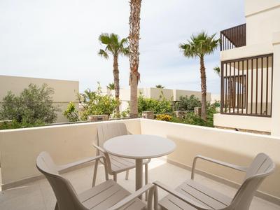 Balcony with white table and chairs, view of palm trees and building facades under clear sky.