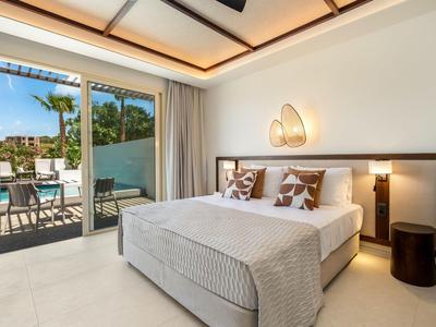 Modern hotel room with double bed and access to terrace overlooking pool.
