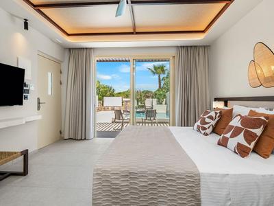 Modern hotel room with large bed, TV, and balcony overlooking palm trees.