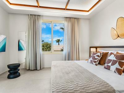 Bright hotel room with large bed, abstract decor, and view of blue sky.