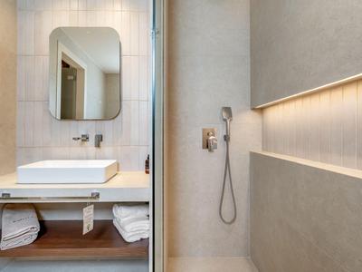Modern hotel bathroom with sink, large mirror, and walk-in shower with handheld showerhead.