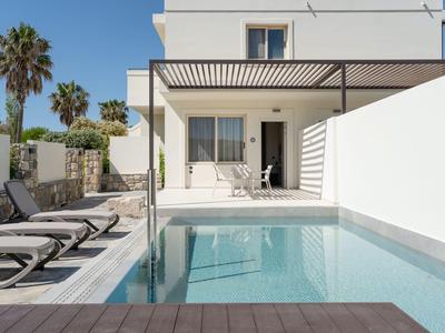 Modern outdoor pool with lounge chairs and terrace of a white hotel.