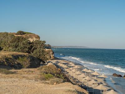 Spiaggia con sabbia, rocce, vegetazione e ombrelloni lungo la costa sotto un cielo sereno.