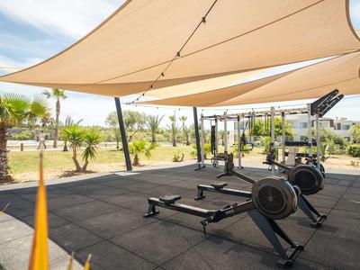 Area fitness all'aperto con vogatori e tende da sole in un ambiente alberghiero verde.