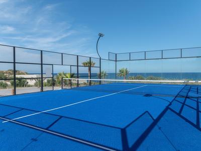 Campo da paddle tennis blu con vista mare e cielo sereno accanto a un complesso alberghiero.