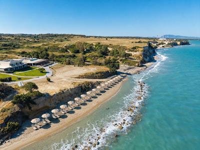 Hotel sulla costa con spiaggia di ciottoli, ombrelloni e acqua azzurra sotto un cielo blu.