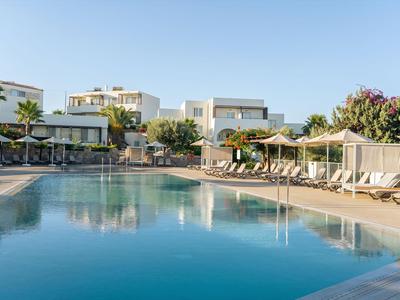 Piscina moderna dell'hotel con lettini e ombrelloni, circondata da edifici bianchi e palme.