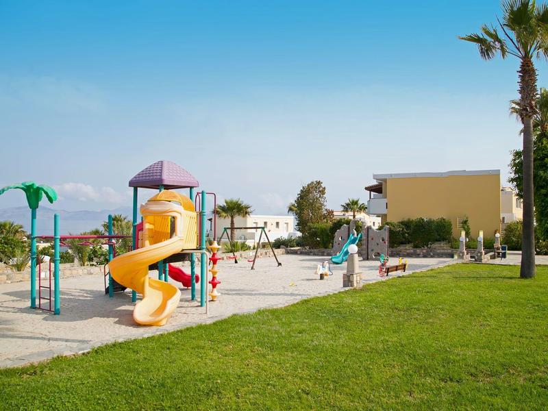 Parque infantil con toboganes y columpios junto a césped y palmeras bajo cielo despejado