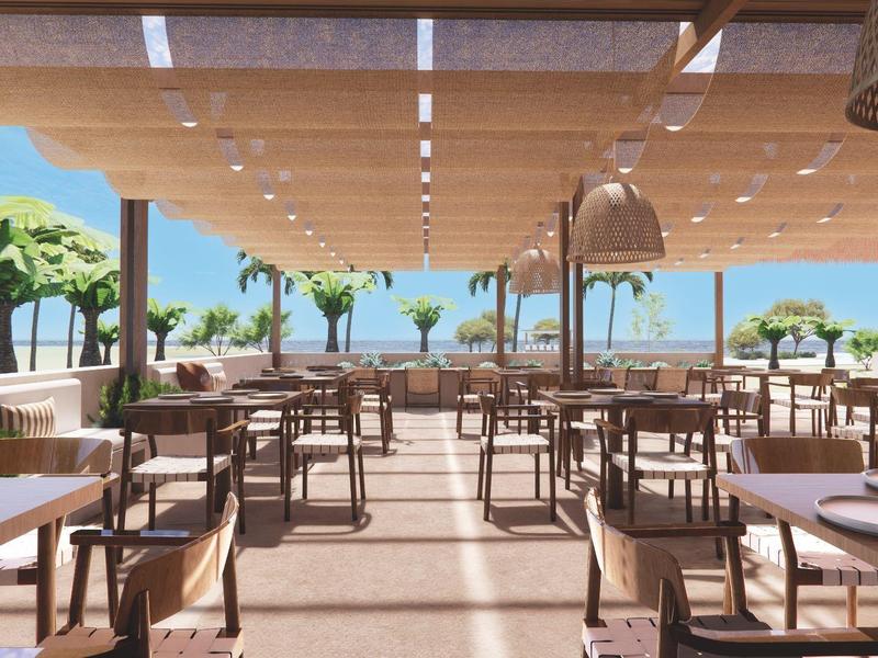 Área de desayuno abierta con mesas de madera y vista al mar.