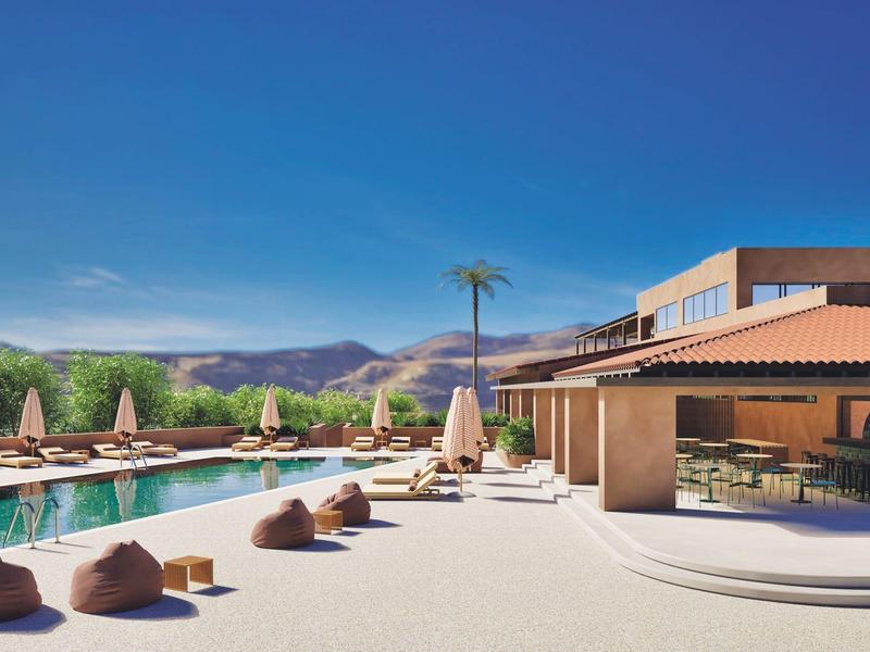 Piscina moderna de hotel con tumbonas y pufs bajo un cielo azul despejado.
