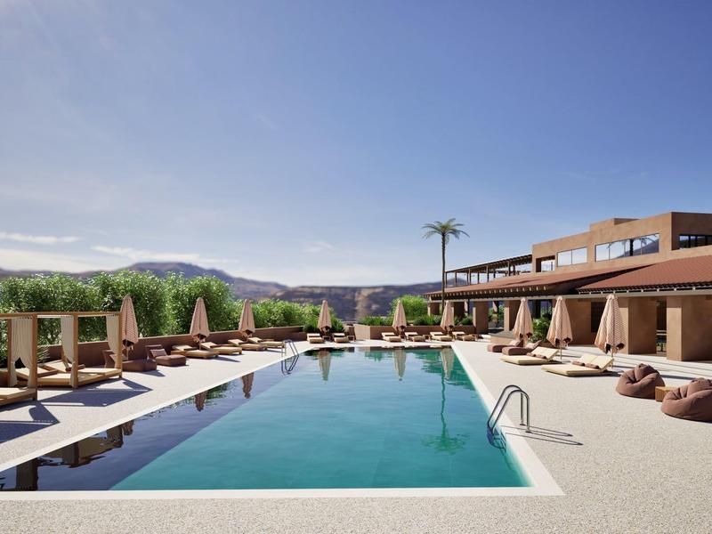 Área de piscina moderna con tumbonas y sombrillas junto al edificio del hotel bajo cielo azul.