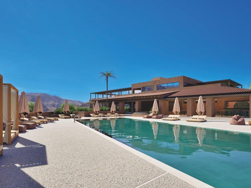 Piscina moderna de hotel con tumbonas y vista a las montañas bajo cielo despejado.