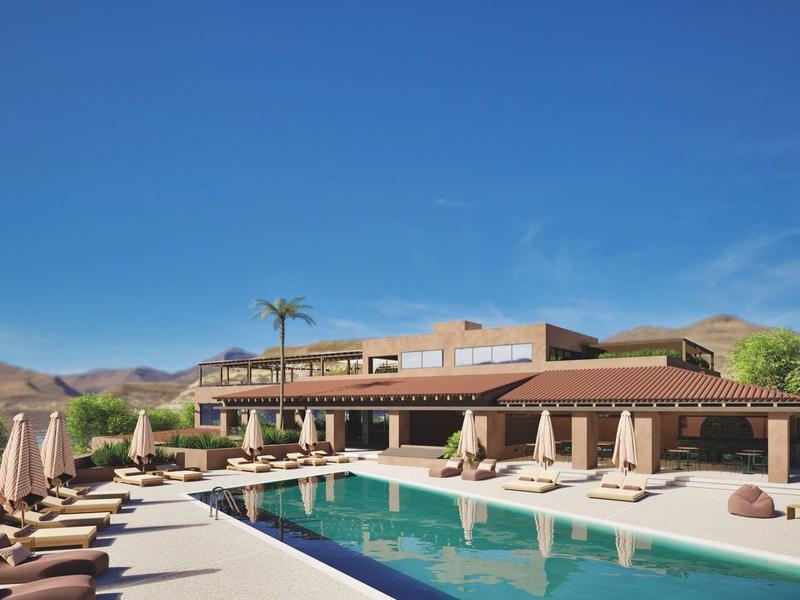 Gran piscina con tumbonas y sombrillas frente a un hotel en un paisaje montañoso soleado