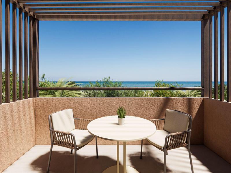 Balcón con mesa redonda, dos sillas y vista al mar bajo un cielo despejado.