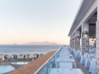 Elegantes Hotelrestaurant mit Terrassenblick auf Meer und Berge bei Sonnenuntergang.