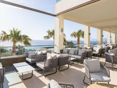 Moderner Außenbereich mit Sesseln und Tischen, Meerblick und Palmen im Hintergrund