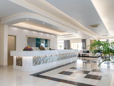 Moderna hall d'hotel con banco reception bianco e area salotto alla luce naturale.