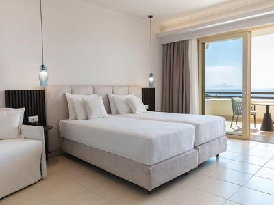 Camera d'hotel luminosa con letto matrimoniale, area salotto e balcone con vista mare.