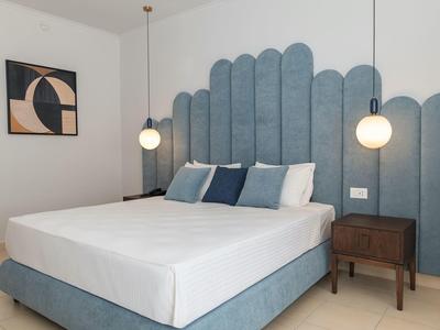 Camera moderna con letto imbottito blu e due comodini con lampade sospese.