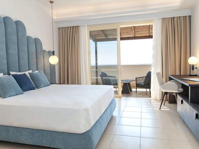 Camera d'hotel luminosa con letto grande, scrivania e balcone con area salotto.