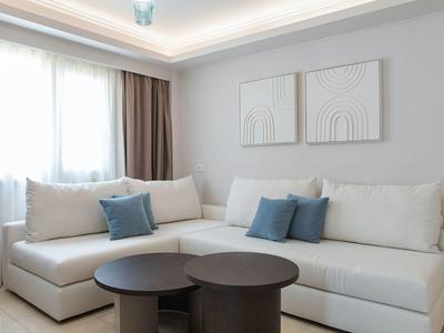 Soggiorno luminoso con divano angolare bianco e due tavoli rotondi scuri.