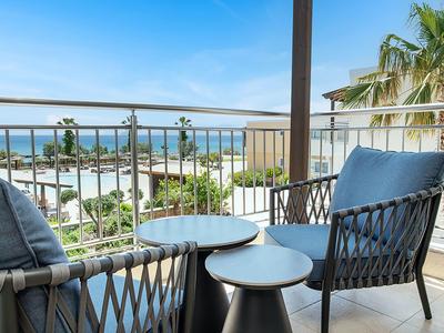 Balcone con due sedie e tavoli con vista sul mare e le palme.