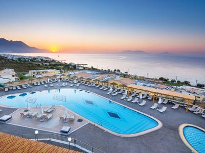 Hotelpool mit Liegestühlen und Meerblick bei Sonnenuntergang.