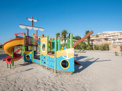Struttura colorata a forma di nave su sabbia sotto un cielo azzurro.