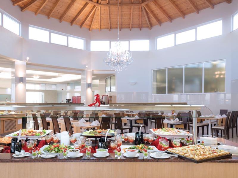 Elegante buffet per la colazione con vari dolci, frutta e bevande calde in una sala da pranzo luminosa.