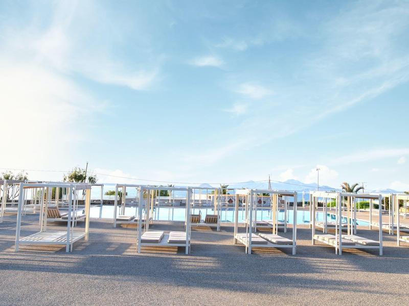 Lettini da spiaggia bianchi vuoti in un ambiente soleggiato e parzialmente nuvoloso.