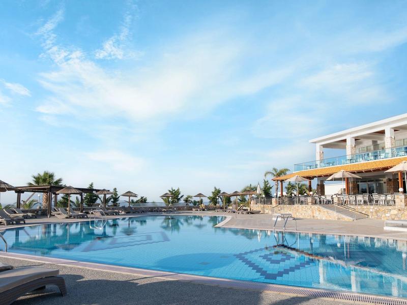 Grande piscina dell'hotel con lettini e palme sotto un cielo azzurro.