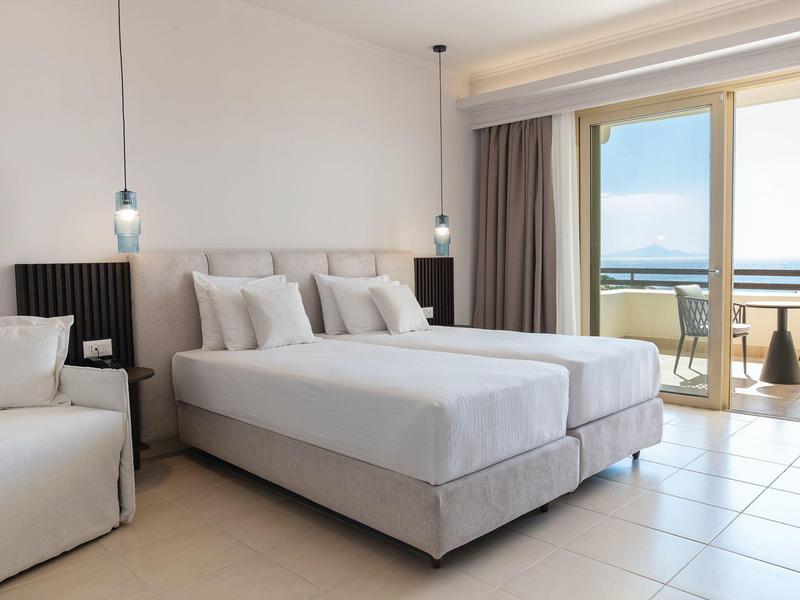 Camera d'hotel luminosa con letto matrimoniale, area salotto e balcone con vista mare.