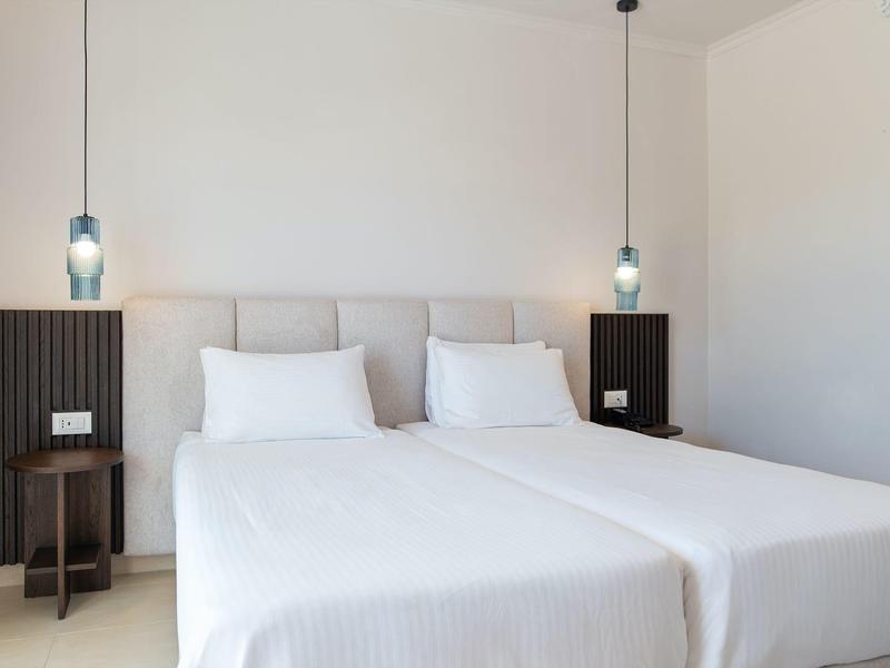 Camera d'hotel minimalista con due letti singoli, biancheria bianca e lampade sospese.