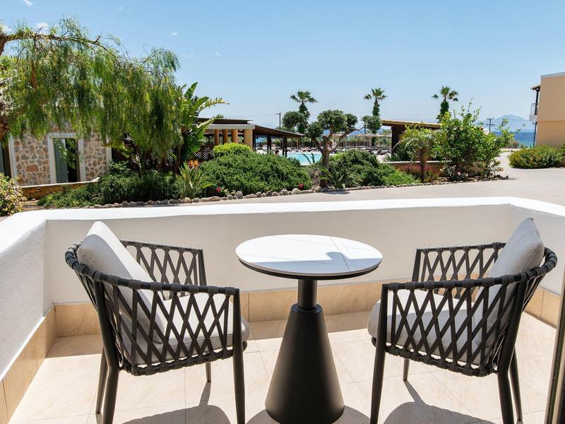 Due sedie e un tavolo su un balcone con vista su un giardino e una piscina.