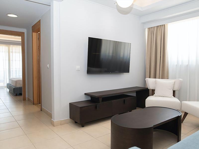 Soggiorno moderno con TV, poltrona e mobili scuri in ambiente luminoso.