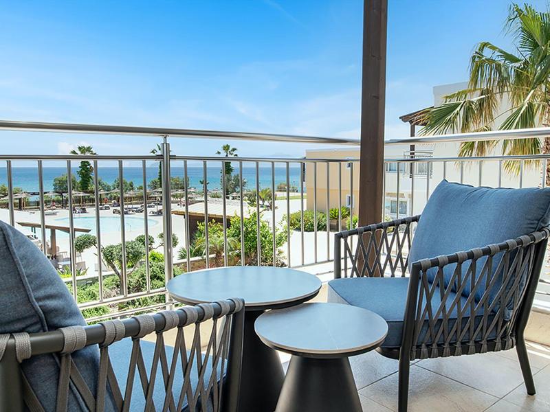 Balcone con due sedie e tavoli con vista sul mare e le palme.