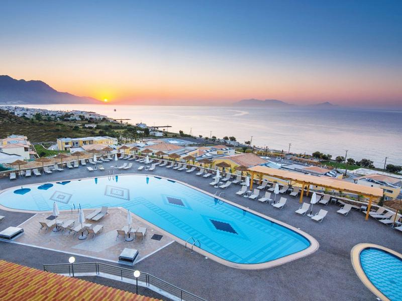 Hotel con grande piscina e lettini a sdraio con vista sul mare al tramonto.