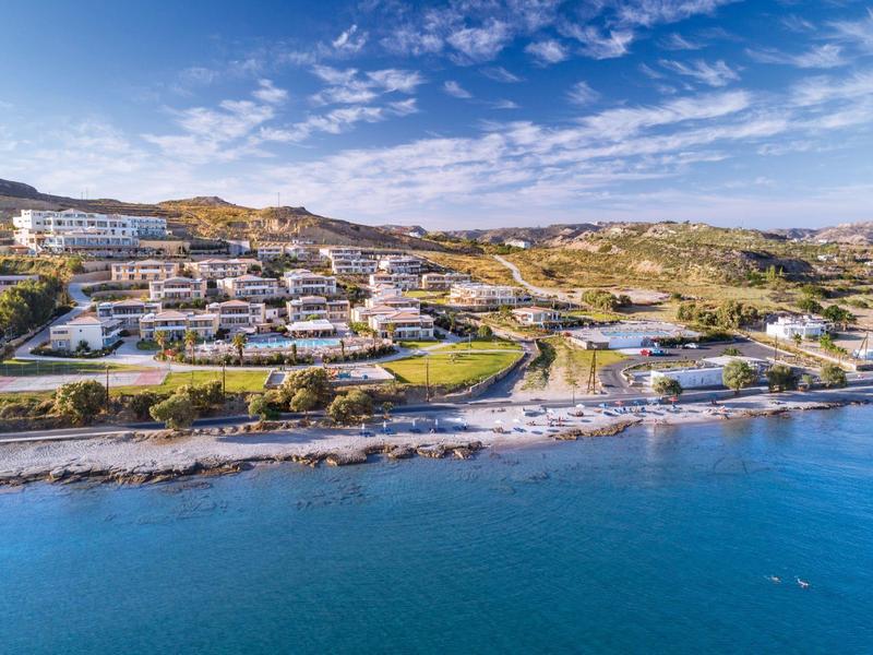 Hotel costiero con edifici bianchi e piscina vicino a costa rocciosa sotto cielo azzurro.